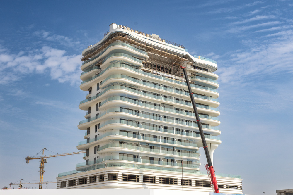 Beach Walk Residence A modern building under construction with a curved facade, featuring large glass windows and scaffolding.